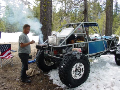 1986 Ford Bronco - A man grills food next to a custom-built off-road vehicle in a snowy, wooded environment.