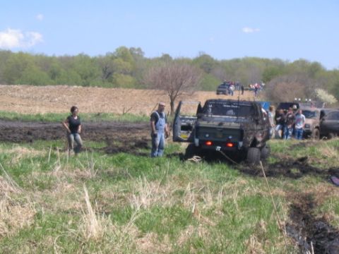 1977 Ford F-150 - Several trucks are stuck in the mud while onlookers observe the scene on a sunny day.