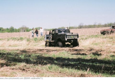 1977 Ford F-150 - A black 1977 Ford F-150 is stuck in a muddy field, with people observing the scene.