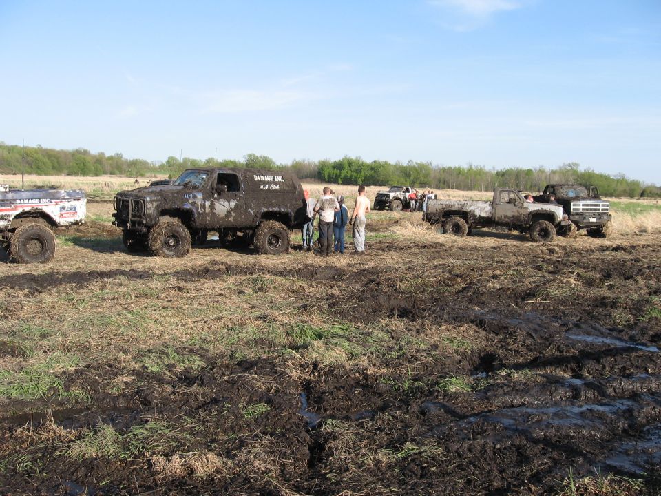 Muddy SUVs and trucks in a field with people standing around