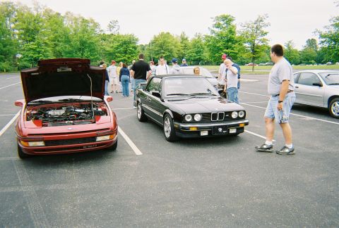 1991 Ford Probe - A red car with its hood open is parked next to a black convertible in a parking lot.