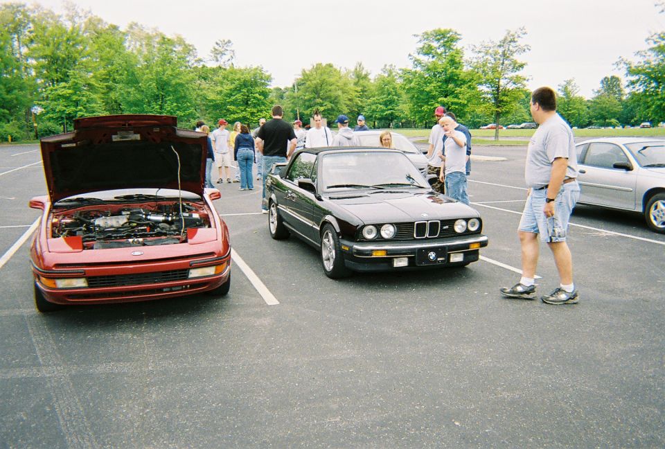 Red car with hood open, front view. Black convertible parked next to it