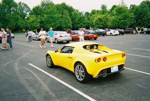 1991 Ford Probe - A bright yellow sports car is parked in a lot with other vehicles and people milling around.