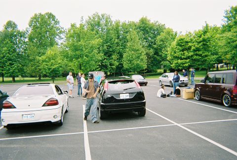 1991 Ford Probe - Several vehicles and people are gathered in a parking lot on a cloudy day.