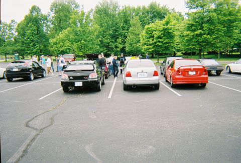 1991 Ford Probe - A collection of vehicles are parked in an outdoor lot, with a group of individuals gathered nearby.