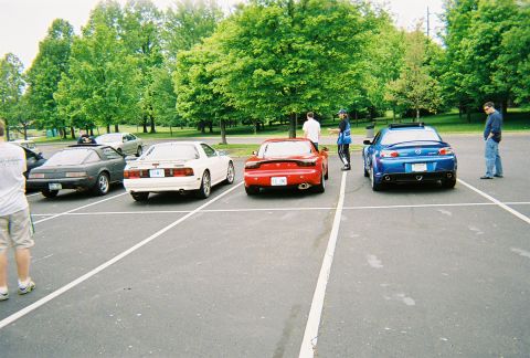 1991 Ford Probe - Several generations of Mazda sports cars are parked in a lot on a sunny day.