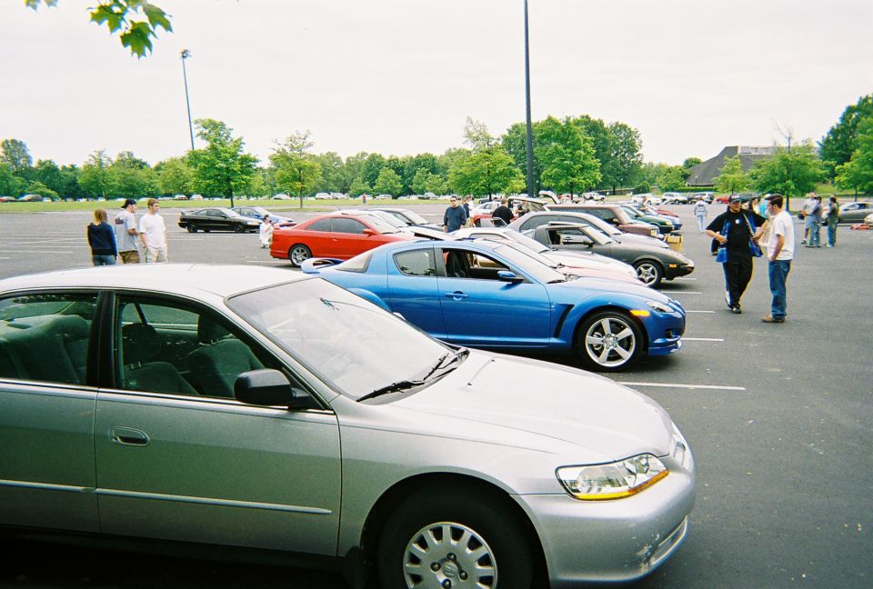 Several cars parked in a lot, with people standing around them