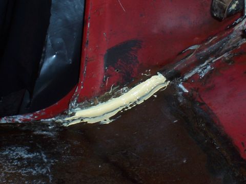 1978 Ford Bronco - Seam sealer is applied to a section of a red vehicle's bodywork.