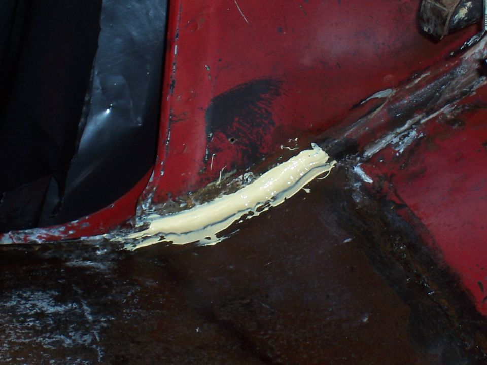 close-up of red car body panel with yellow sealant applied to a seam