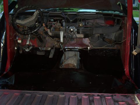 1978 Ford Bronco - The interior of a vehicle shows exposed wiring and a bare floor, with the red exterior visible.