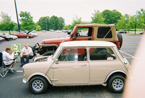 1991 Ford Probe - Two vehicles, a classic Mini Cooper and a Jeep Wrangler, are parked in a lot with people nearby.