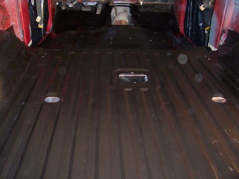 1978 Ford Bronco - The interior floor of a red vehicle, a ribbed metal surface and visible floor mounts.