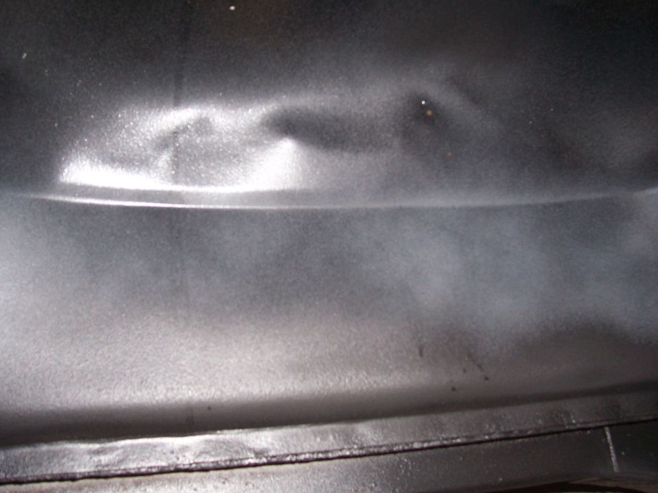 Close-up of a dented, dark-colored metal panel with a horizontal crease