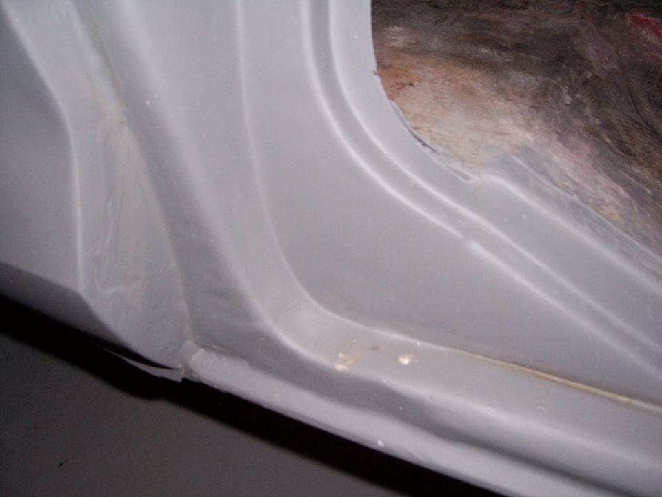 Close-up of a vehicle's inner door jamb, showing primer and some rust