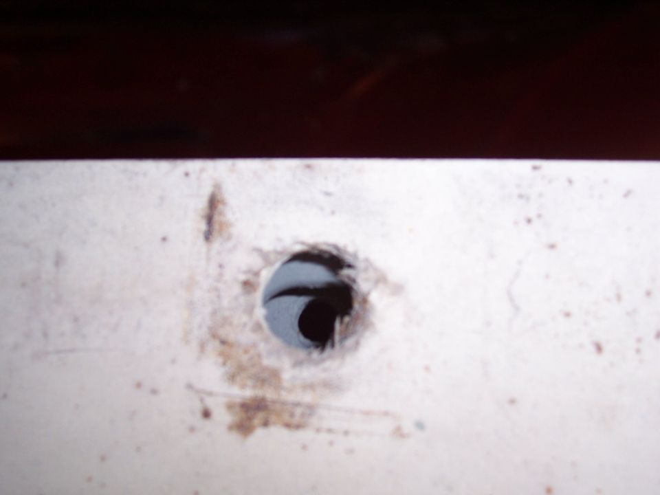 Close-up of a hole drilled into a white panel, with some dirt smudges. Supermotors.net logo visible