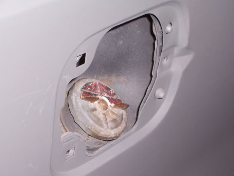 1978 Ford Bronco - Close-up of an open fuel filler door on a gray vehicle, showing the metal cap inside.