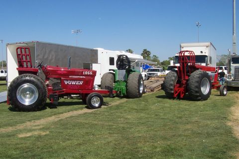 1994 Ford F-150 - Modified tractors are lined up on a grassy field, with trailers and trucks in the background under a clear blue sky.
