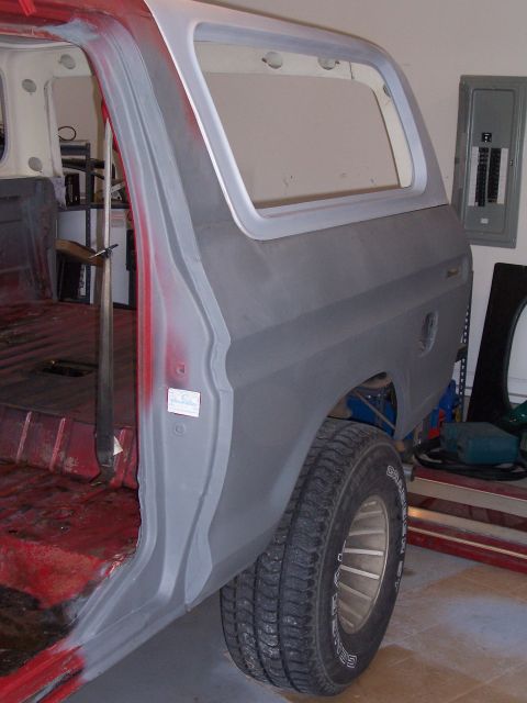1978 Ford Bronco - The rear quarter panel of a 1978 Ford Bronco is shown in gray primer, revealing its interior and a garage setting.