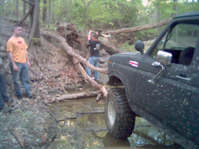 Black Ford Bronco navigating a muddy, wooded trail with fallen trees