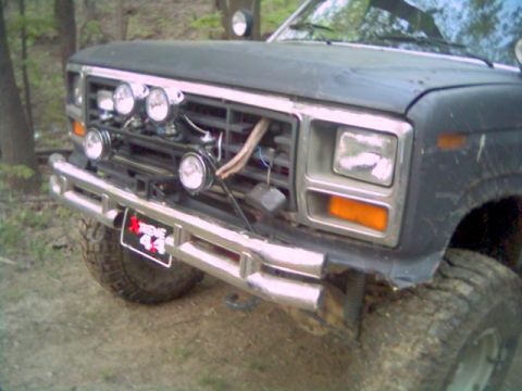 1986 Ford Bronco - Front view of a dark colored truck with a chrome bumper and grille, auxiliary lights and a custom license plate.