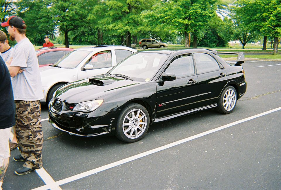 Black sedan with a rear spoiler and hood scoop, parked in a lot