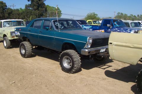 1994 Ford F-150 - A teal sedan with a lifted suspension and oversized tires is parked outdoors.