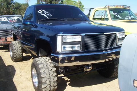 1994 Ford F-150 - A lifted blue pickup truck is parked outdoors, with other vehicles visible in the background.