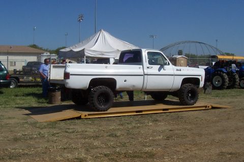 1994 Ford F-150 - A white pickup truck is positioned on a scale, with a clear blue sky overhead and tents in the background.