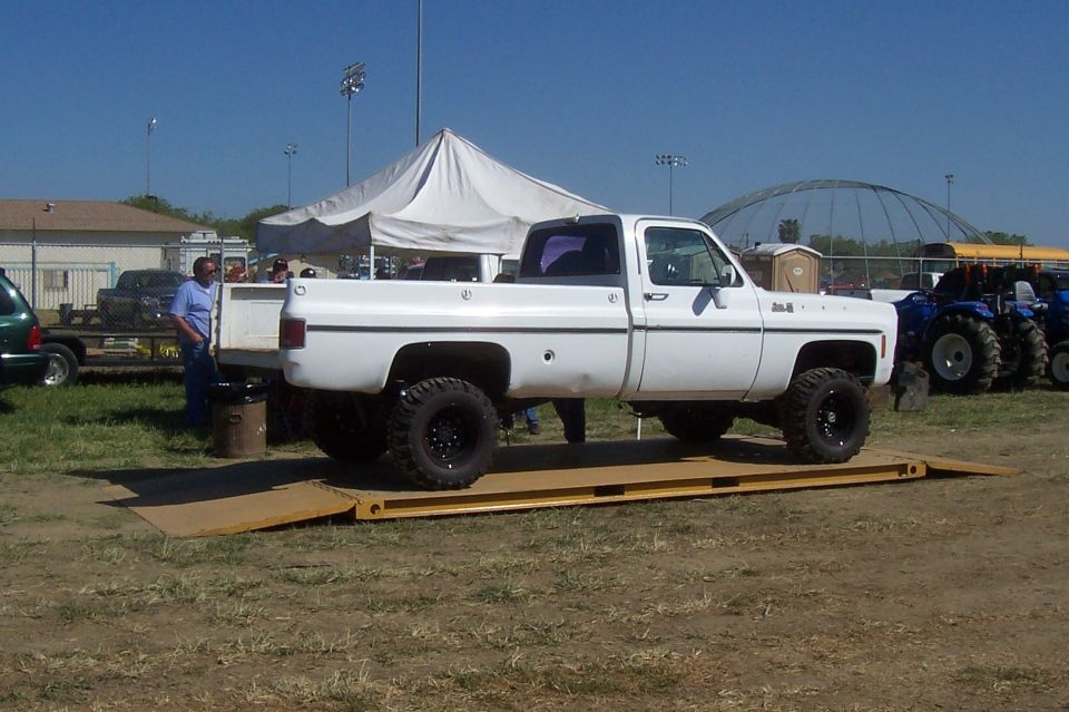 White pickup truck on a scale, side view. It has large tires and a lifted suspension