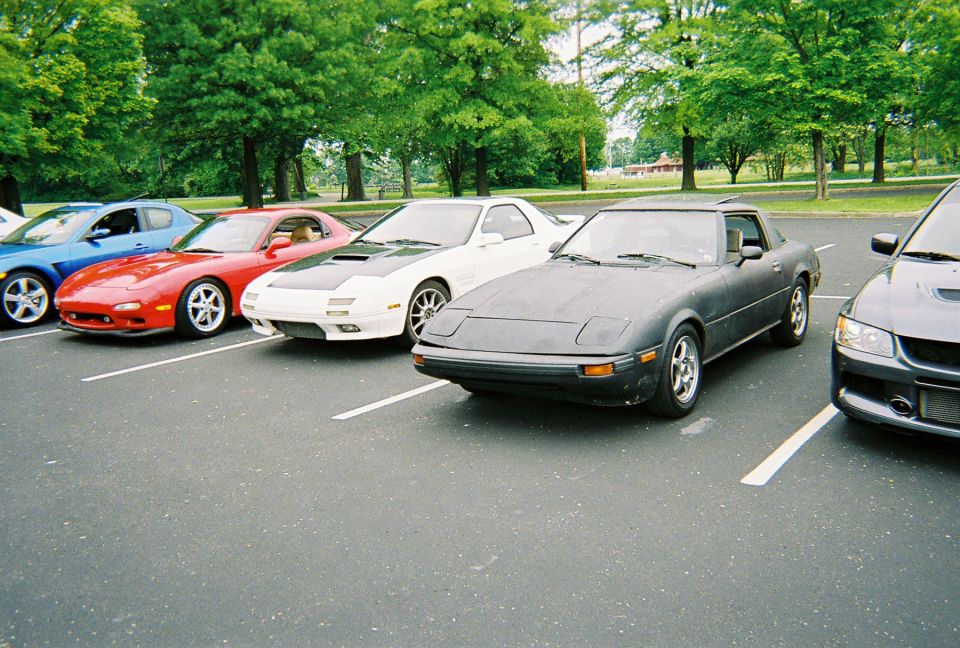 Dark gray Mazda RX-7 parked in a lot with other cars. It has pop-up headlights