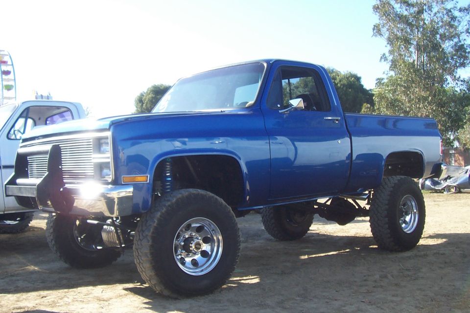 Blue pickup truck with lifted suspension and large tires, seen from a 3/4 front angle