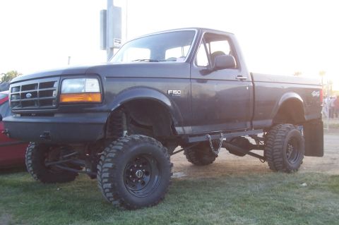 1994 Ford F-150 - This lifted 1994 Ford F-150 pickup truck is shown in a three-quarter front view, parked on grass.