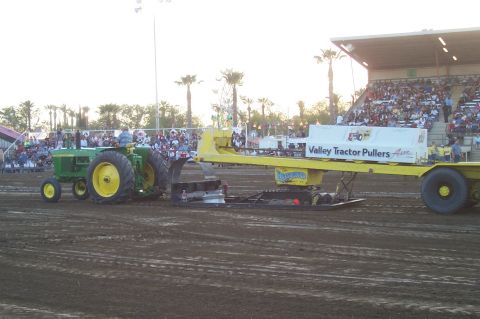 1994 Ford F-150 - A green tractor competes in a tractor pull event, dragging a weighted sled in front of a crowd.