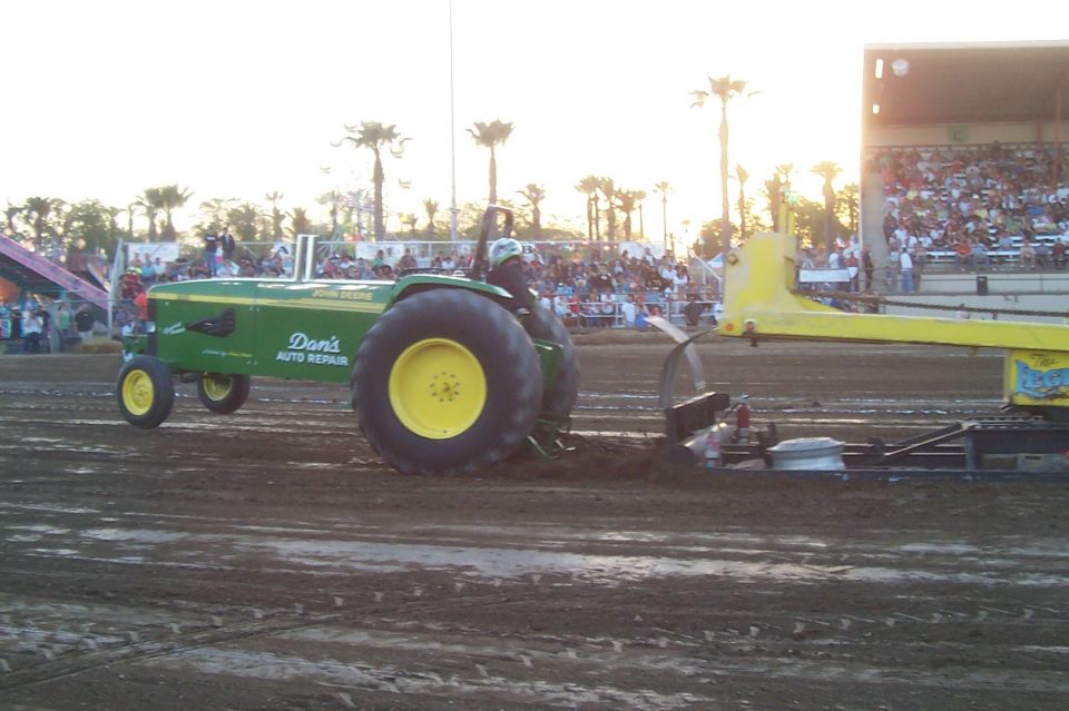 Green John Deere tractor with yellow wheels pulling a sled on a dirt track