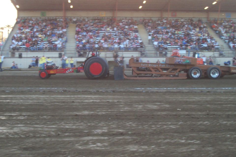 Tractor pulling a sled at a competition with spectators in the background