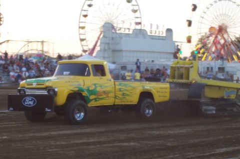 1994 Ford F-150 - A vintage yellow Ford pickup truck with custom flames is seen pulling a sled at an outdoor event with carnival rides in the background.