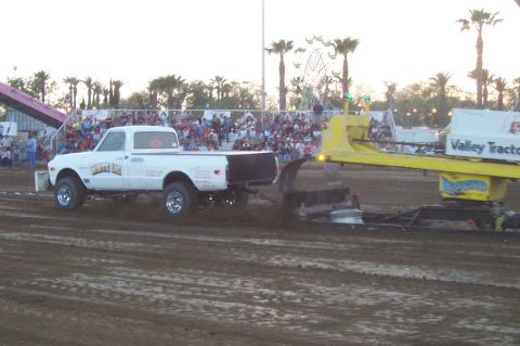 1994 Ford F-150 - A classic Chevrolet C10 pickup truck competes in a pull event, with spectators and a Ferris wheel in the background.