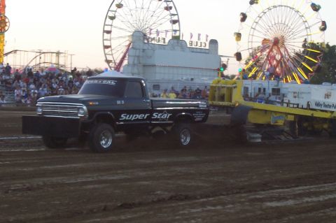 1994 Ford F-150 - A modified Ford F-Series truck competes in a pull event at a fairground, with amusement rides visible in the background.