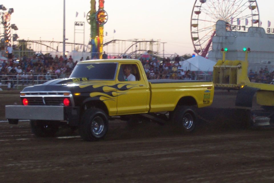 Yellow pickup truck with black flame decals and a lifted suspension, pulling a trailer at a fairground