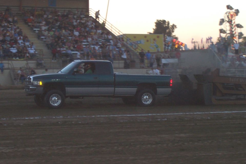 Green and silver Dodge Ram pickup truck pulling a sled at a pull event. Crowd in bleachers