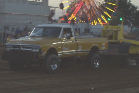 1994 Ford F-150 - A lifted yellow 1971 GMC pickup truck with a plow is seen at an outdoor event with a Ferris wheel in the background.