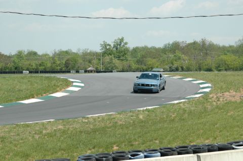 1993 Ford Mustang - A blue Ford Mustang navigates a turn on a race track during a sunny day.
