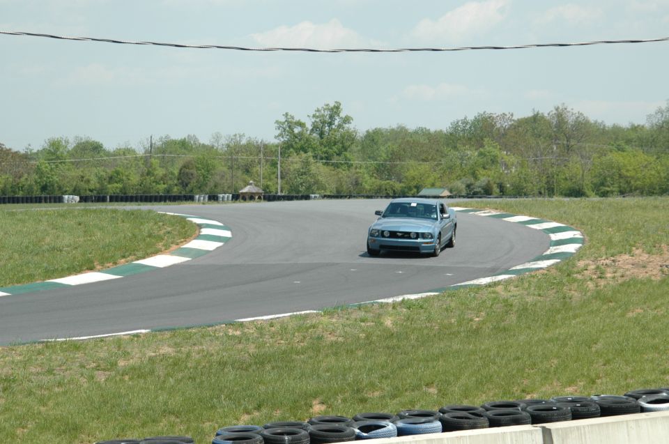 Blue Ford Mustang on a race track, front view. Model appears to be from the 2005-2014 generation