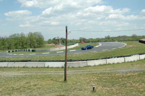 1993 Ford Mustang - A blue sports car navigates a turn on a race track under a partly cloudy sky.