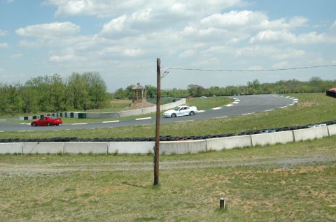 1993 Ford Mustang - A white 1993 Ford Mustang navigates a turn on a race track, with a red car visible in the background.