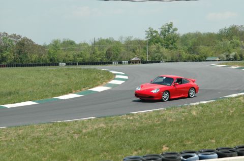 1993 Ford Mustang - A red Porsche 911 navigates a turn on a race track during the day.