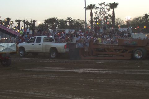 1994 Ford F-150 - A white pickup truck tows a trailer during an event, with spectators and a Ferris wheel visible.