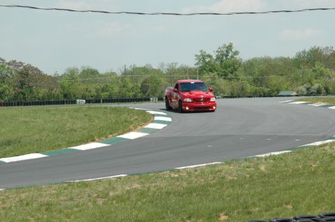 1993 Ford Mustang - A red pickup truck navigates a turn on a race track during the daytime.