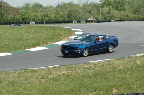 1993 Ford Mustang - Blue Ford Mustang navigates a turn on a race track, with another vehicle visible in the background.