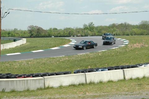 1993 Ford Mustang - A black 1993 Ford Mustang navigates a turn on a race track, with other vehicles in the background.